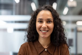 Young curly-haired businesswoman smiling confidently at camera in a modern office headshot