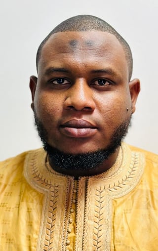 Portrait of a man with a short haircut and beard wearing a yellow embroidered traditional garment against a white background